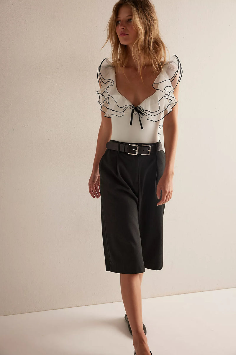 White bodysuit with ruffled black trim and a plunging neckline, paired with high-waisted, wide-leg black pants, perfect for Long Island boutique fashion.