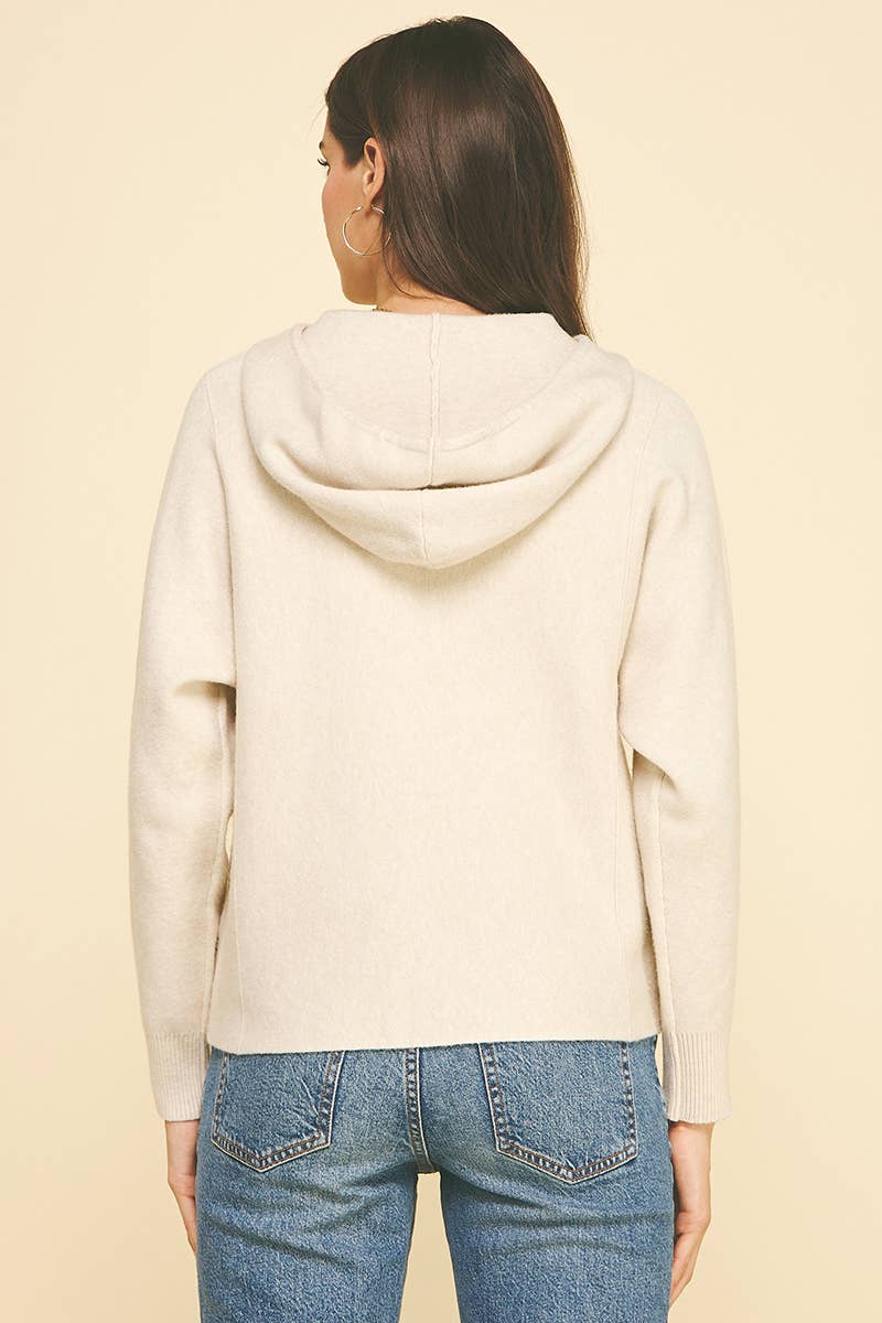 Person wearing a cream hoodie and blue jeans on a beige background