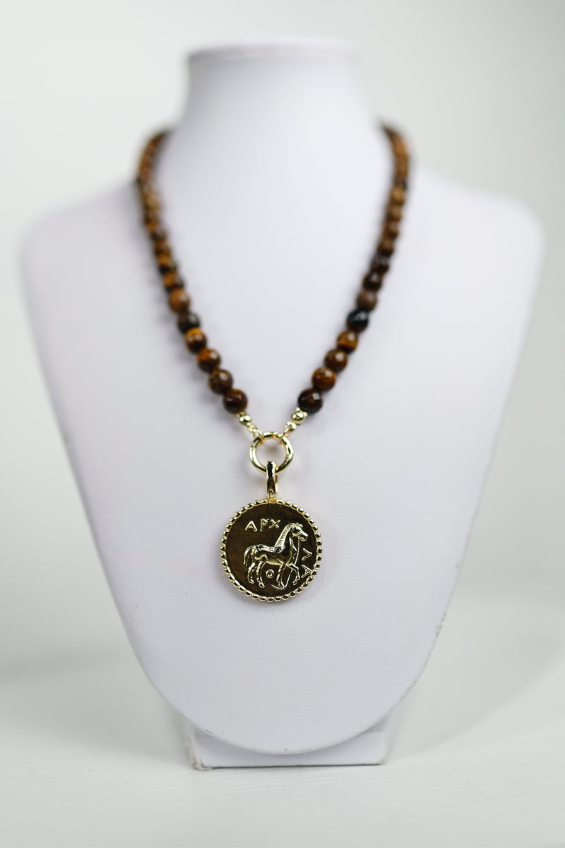 A stunning golden horse medallion pendant hangs from a beaded necklace, perfect for adding style to any look in Long Island boutique fashion.