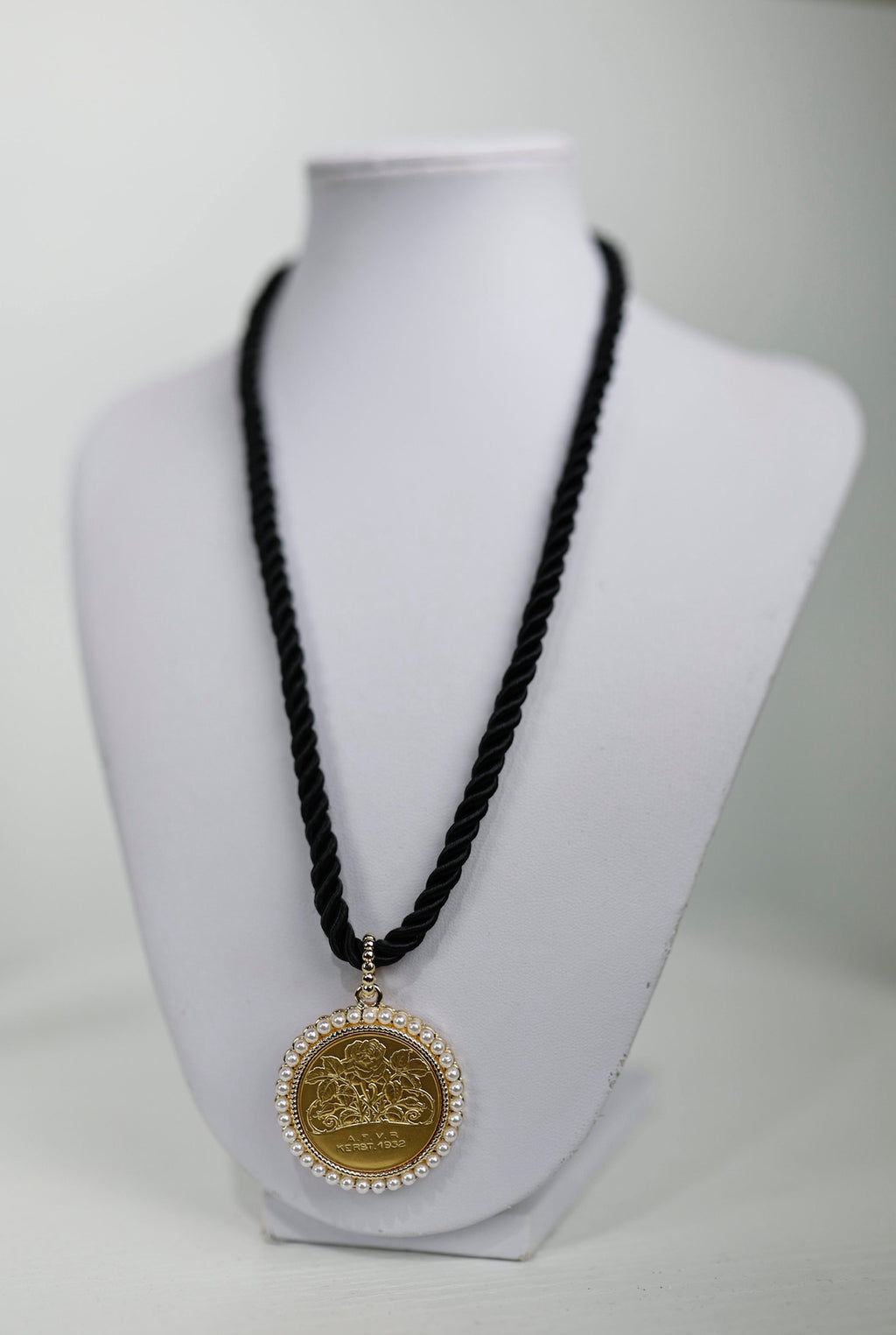 Gold medallion pendant featuring a rose design, surrounded by pearls, on a twisted black cord, perfect for Long Island boutique fashion.