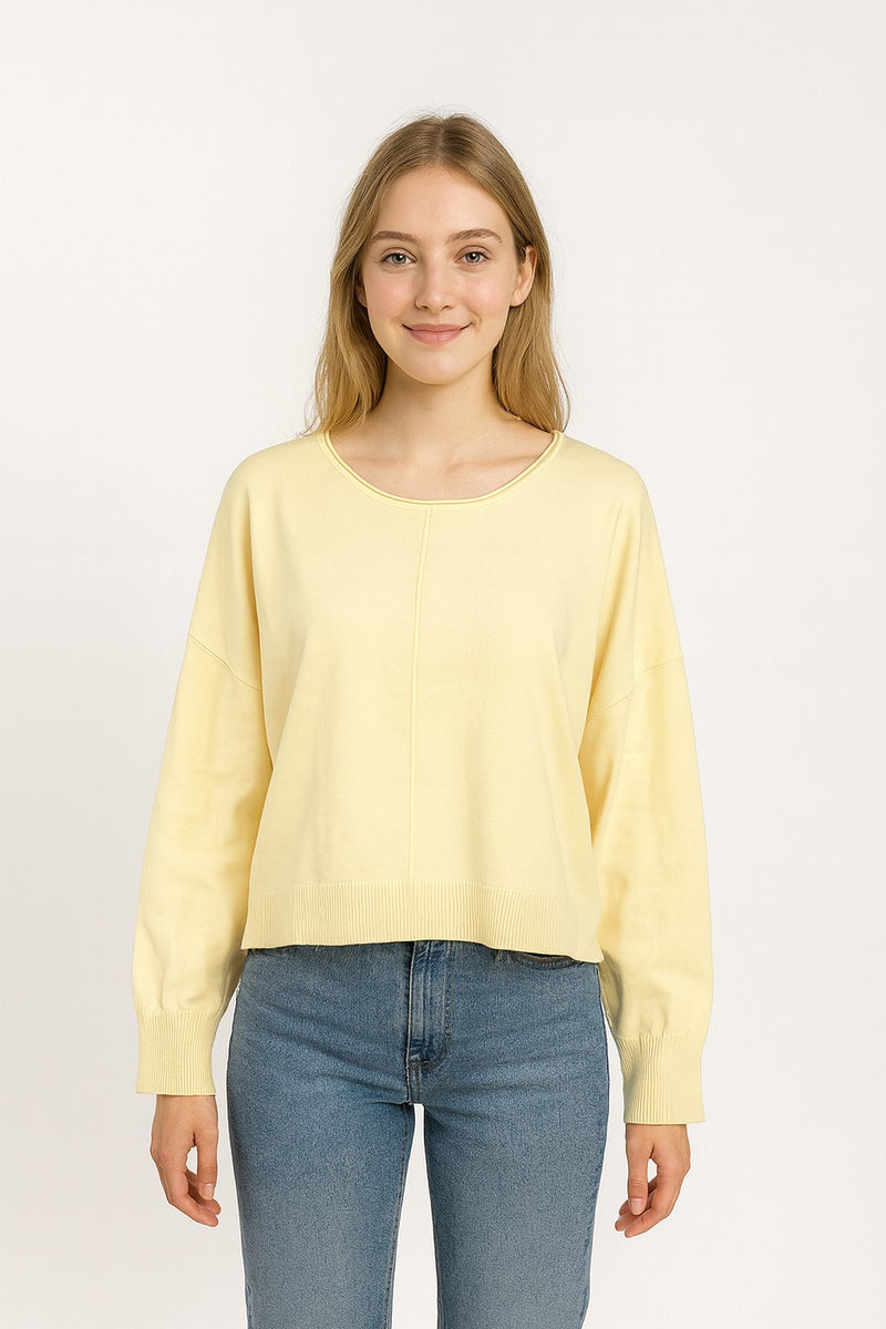 Woman wearing a light yellow sweater and blue jeans on a white background