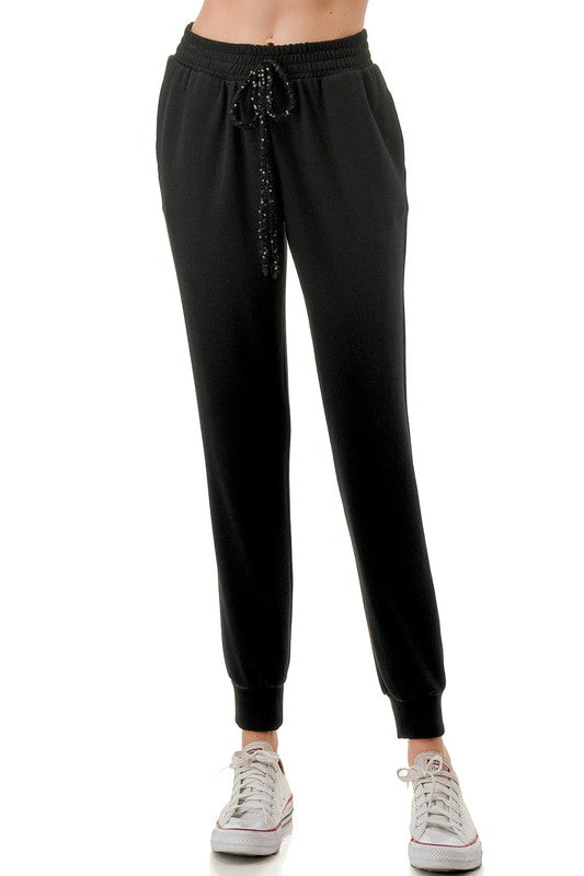 Black jogger pants featuring a comfortable fit, sequin drawstring detail, and ribbed cuffs for a stylish touch in Long Island boutique fashion.
