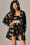 Soft black fleece 3-piece pajama set featuring a hooded cardigan, crop top, and shorts adorned with playful white bow patterns, perfect for cozy nights in at a Long Island boutique fashion destination.