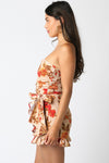 Strapless floral romper featuring a fitted bodice, soft ruffles, and a flattering bow tie at the waist, perfect for Long Island boutique fashion.
