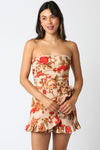 Strapless floral romper in soft beige with vibrant orange and red roses, featuring a ruffled hem and tied waist for chic Long Island boutique fashion.