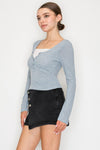 Light blue half-button long sleeve crop top with fitted ribbed texture, paired with a high-waisted black skirt, reflecting Long Island boutique fashion.