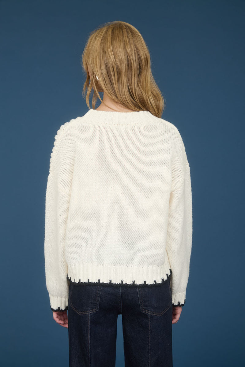 A cozy cream sweater featuring cable knit detailing along the trim, perfect for stylish layering in Long Island boutique fashion.