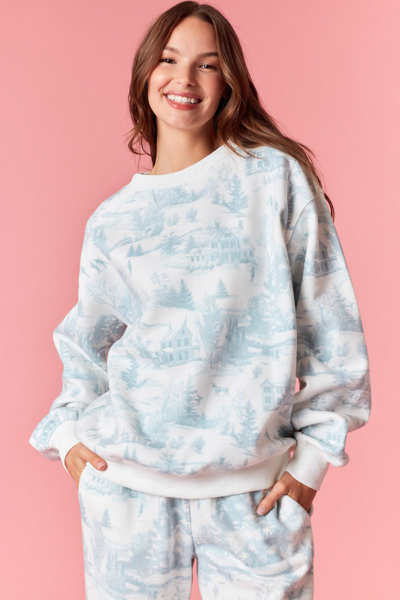 Model wearing Holiday Scenery Print Fleece Terry Sweatshirt in dusty blue — soft pullover with winter village print, available at TandyWear Boutique in Commack, NY. front view