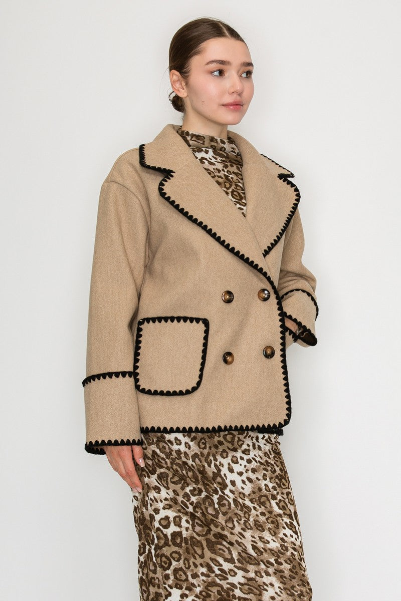 Chic double-breasted jacket in soft beige with contrasting black blanket stitch details and bold buttons, perfect for Long Island boutique fashion.