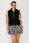 Sleek black front zip knitted vest featuring side pockets, styled over a plaid skirt, perfect for Long Island boutique fashion.