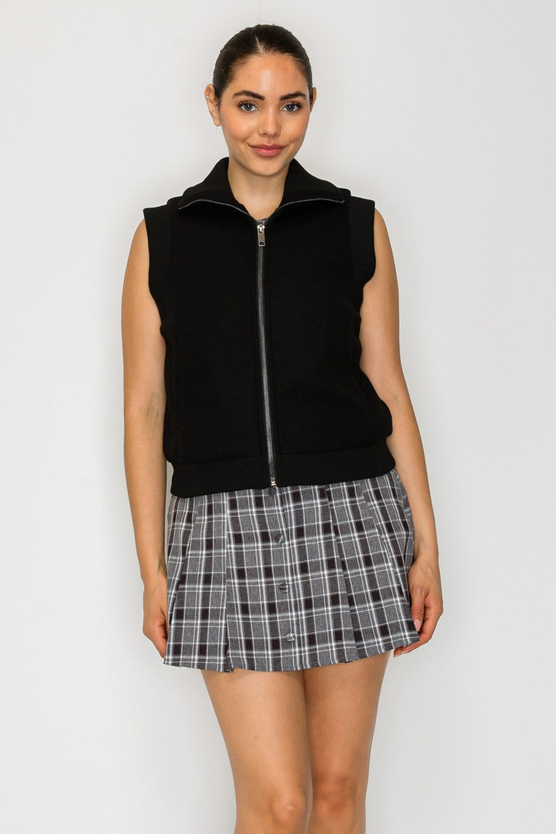 Sleek black front zip knitted vest featuring side pockets, styled over a plaid skirt, perfect for Long Island boutique fashion.