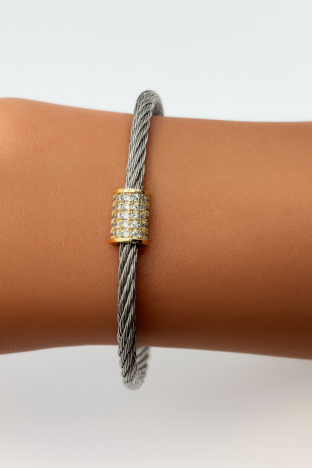 Silver-tone twisted cable bracelet with gold-plated pavé crystal barrel charm on wrist, modern and elegant jewelry style.