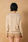 Beige V-neck sweater with a relaxed fit and ribbed cuffs, perfect for chilly days in Long Island boutique fashion.