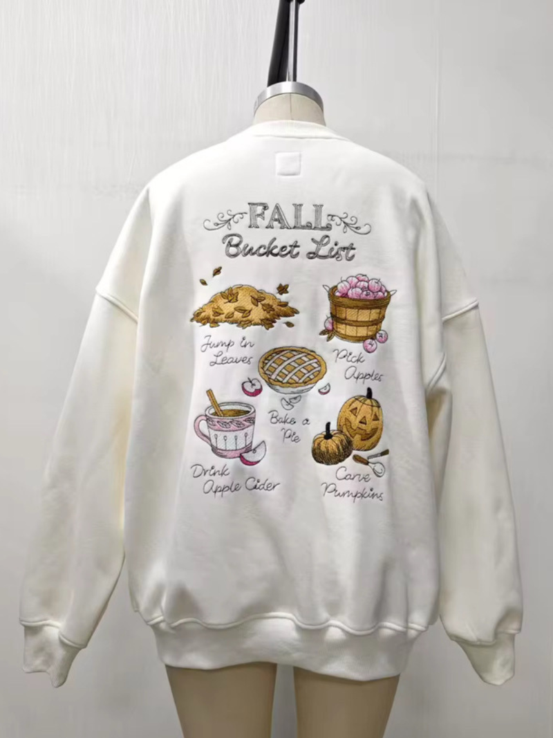 Cream-colored oversized sweatshirt featuring whimsical embroidered graphics of a fall bucket list, ideal for cozy Long Island boutique fashion.