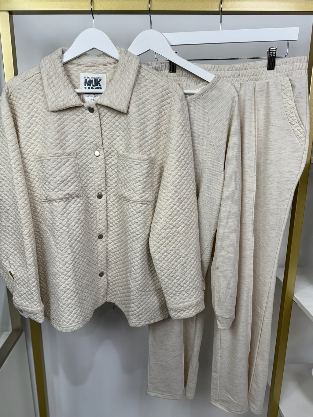 Three-piece oatmeal lounge set with quilted jacket, waffle top, and pants hanging on display