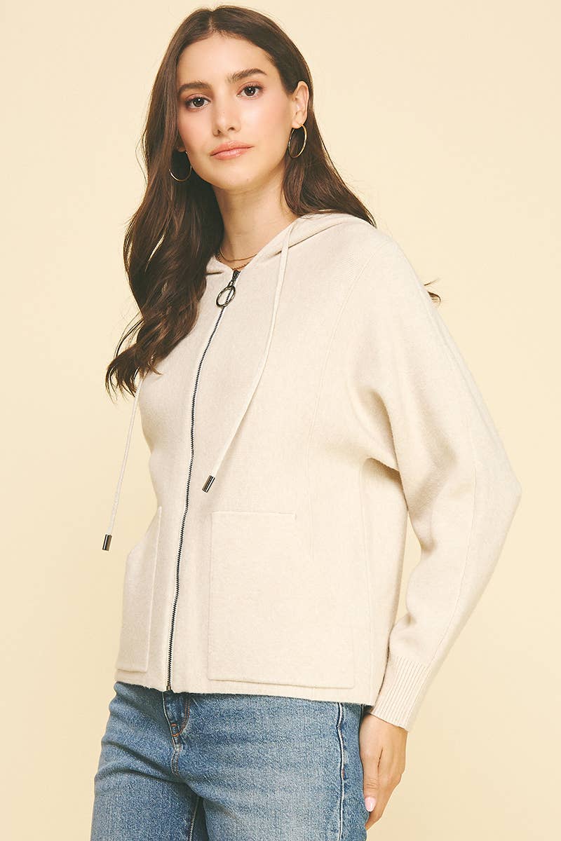 Woman wearing a beige hoodie and blue jeans against a beige background