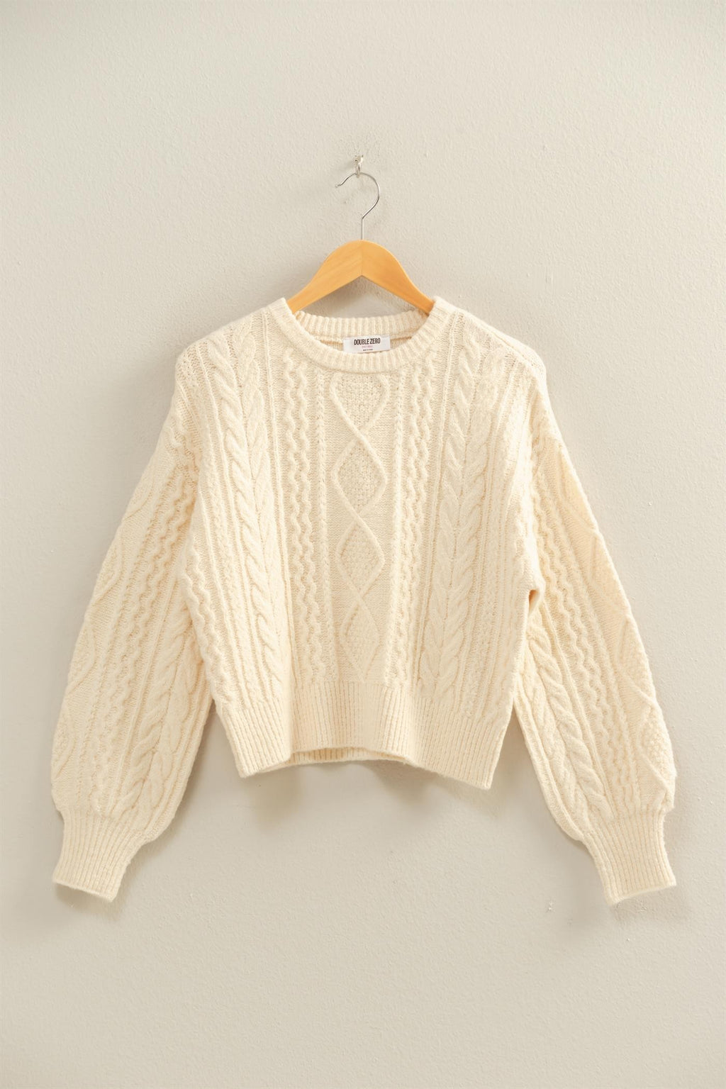 Cream-colored cable knit balloon sleeve sweater with ribbed cuffs and a relaxed fit, perfect for cozy Long Island boutique fashion.
