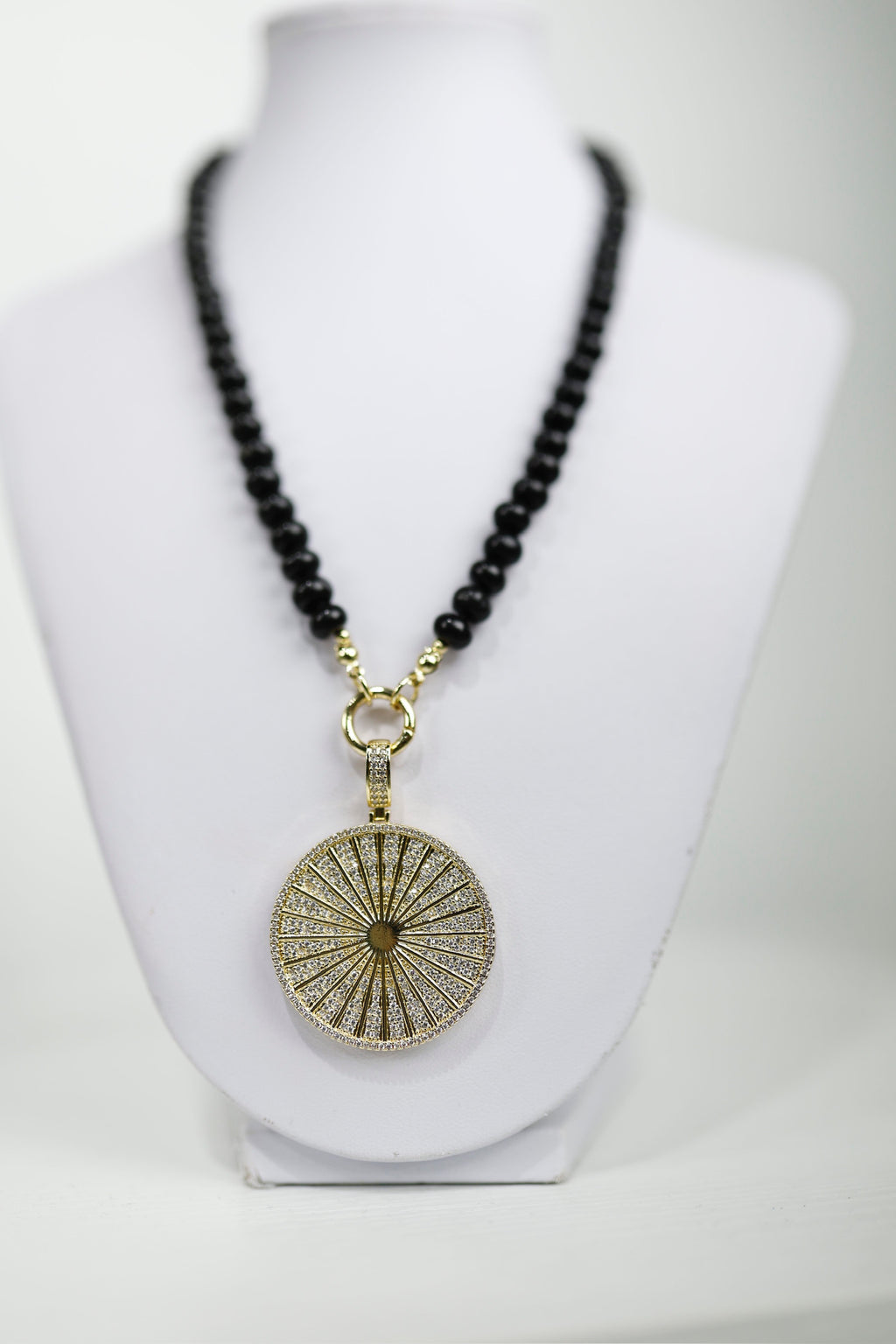 A striking gold medallion necklace with a sunburst design, featuring black beaded accents, perfect for Long Island boutique fashion.