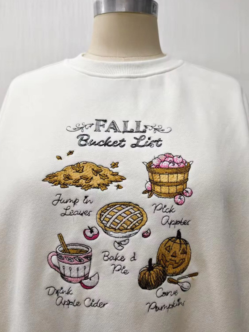 Cream sweatshirt featuring playful embroidered designs of autumn activities, ideal for a cozy look from a Long Island boutique fashion.