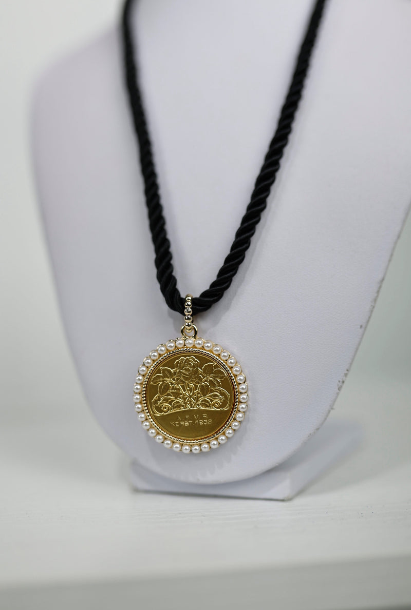 Gold medallion pendant featuring a rose design, surrounded by pearls, on a twisted black cord, perfect for Long Island boutique fashion.