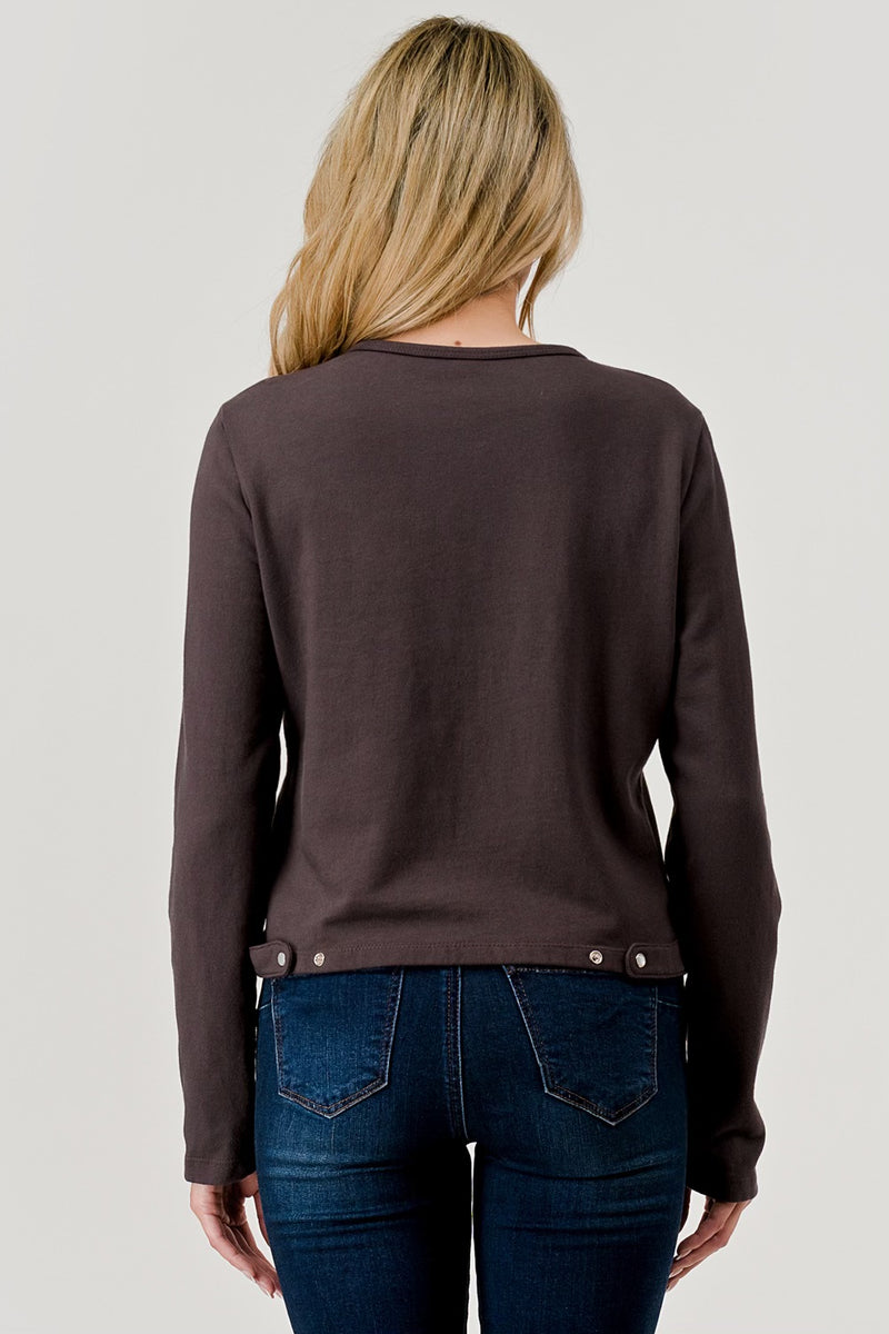 Person wearing a brown long-sleeve shirt with button details on a plain background