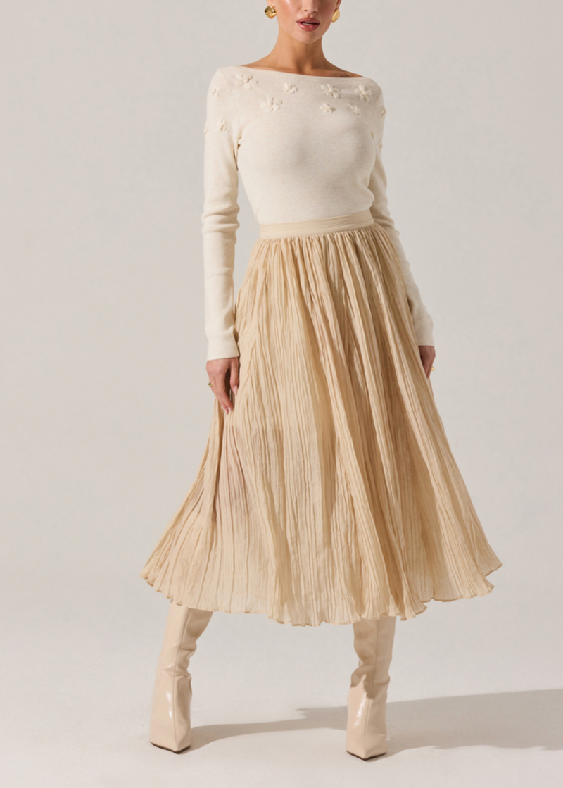 Cream-colored fitted sweater with floral embellishments, paired with a flowing pleated beige skirt, embodying elegant Long Island boutique fashion.