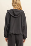 Casual chic zip front hoodie in solid black with a relaxed fit and drawstring hood, perfect for Long Island boutique fashion.