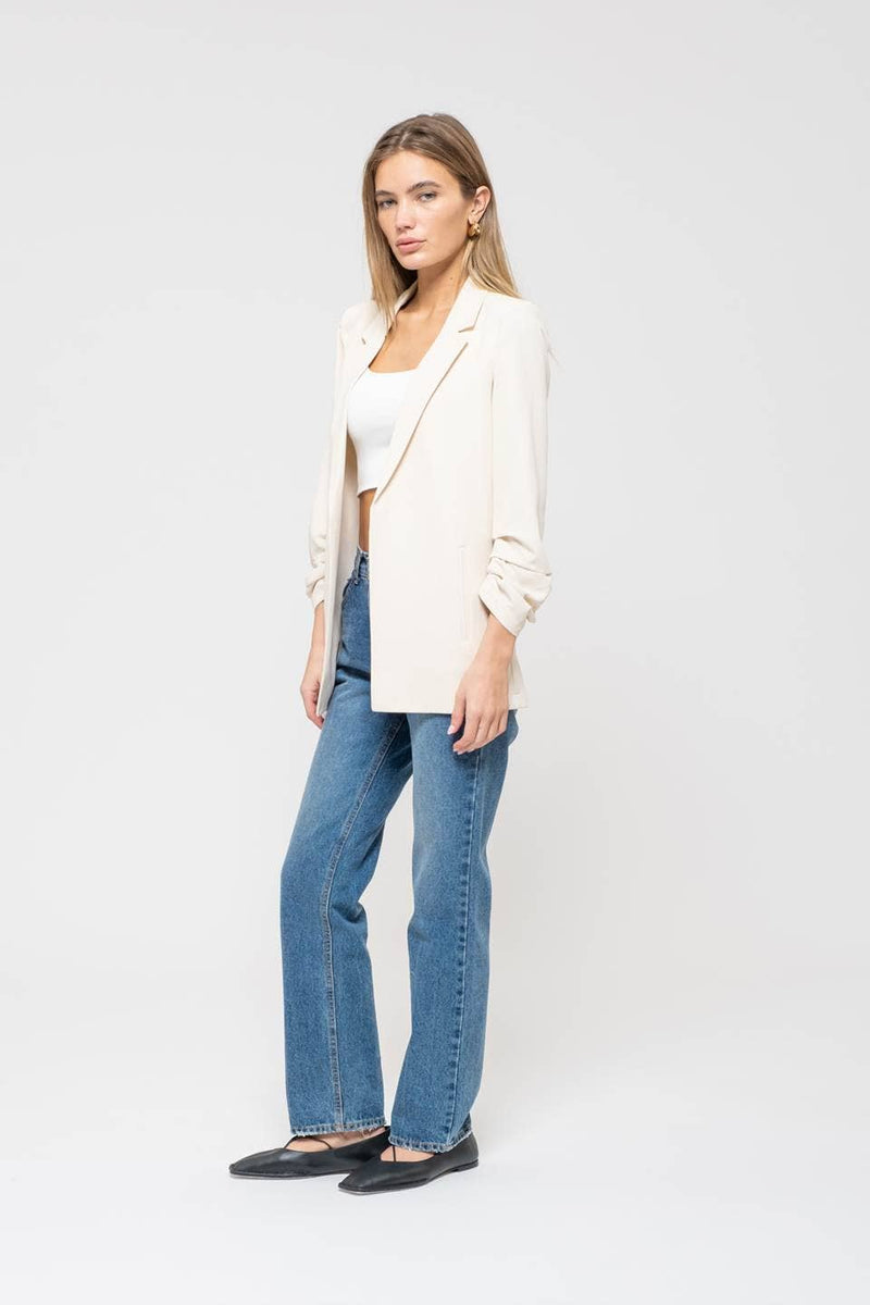 Light beige 3/4 ruched sleeve blazer styled over a cropped white top and high-waisted blue jeans, perfect for Long Island boutique fashion.