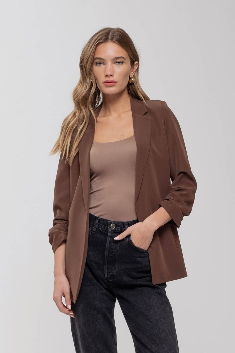 Chic brown 3/4 ruched sleeve blazer paired with a nude top and black high-waisted jeans, perfect for Long Island boutique fashion.