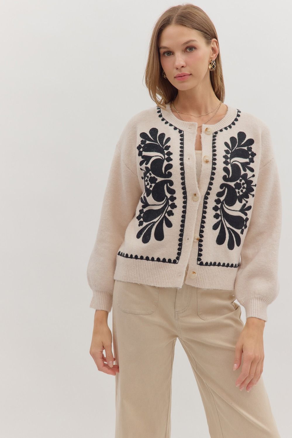 Soft beige sweater knit cardigan features intricate black floral embroidery and button closure, showcasing stylish Long Island boutique fashion.