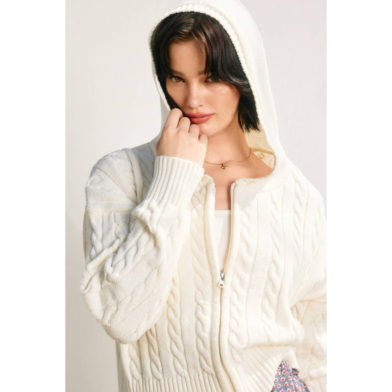 Cozy cable knit cardigan in soft cream, featuring a hood and full zip, perfect for stylish layering in Long Island boutique fashion.