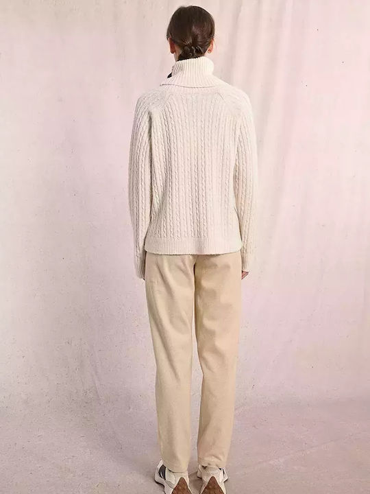 Chunky cable knit turtleneck sweater in a soft cream color, paired with relaxed beige trousers, perfect for cozy Long Island boutique fashion.