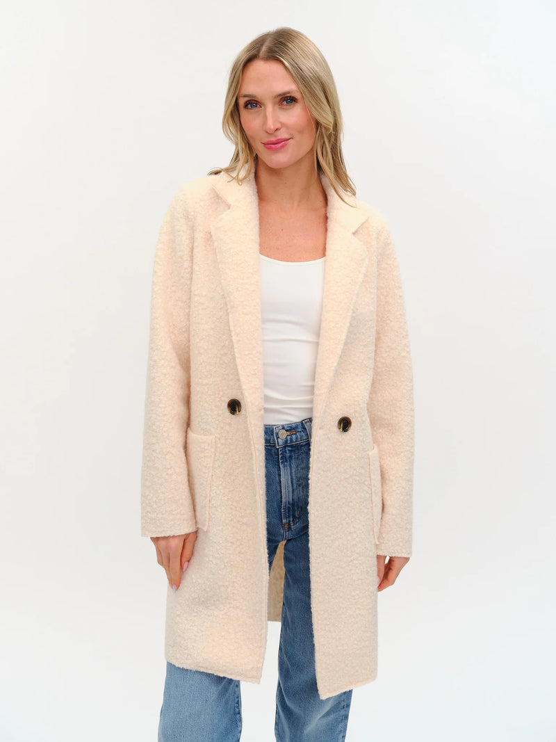 Elegant faux shearling long coat in soft cream with a tailored fit, featuring a double-button front and practical pockets, perfect for Long Island boutique fashion.
